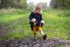 Young girl outside in coat and rainboots, lifting up her foot and stomping in the mud 
